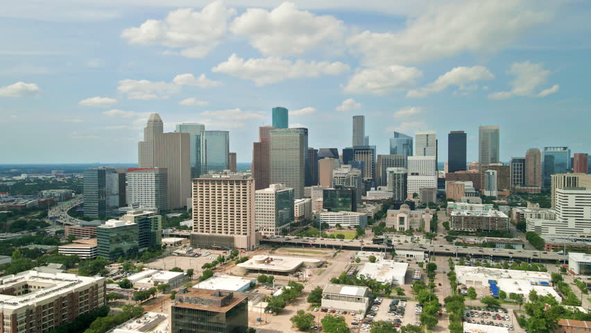Aerial drone view circling the Downtown Houston skyline, showcasing modern skyscrapers and office towers beneath dramatic clouds during daytime in Houston, Texas, USA.