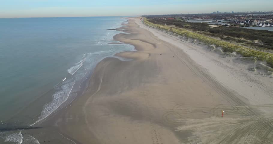 An aerial overflight of a long sandy beach with dunes and gentle waves along the coast of the Netherlands