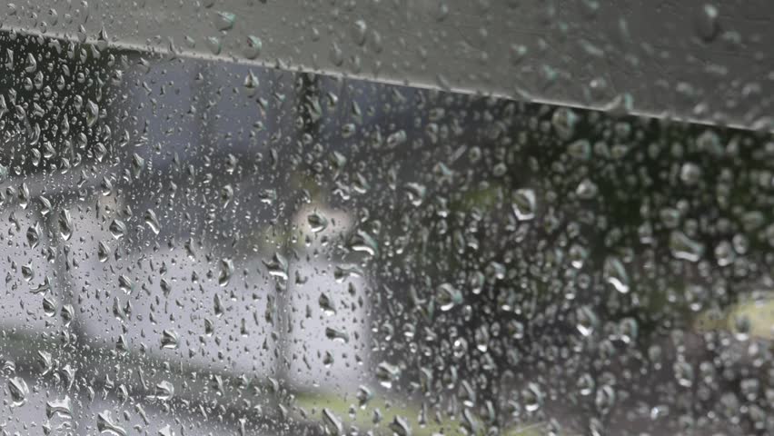 Blurry raindrops on a building window with cars moving along wet roads in Lisbon, Portugal.