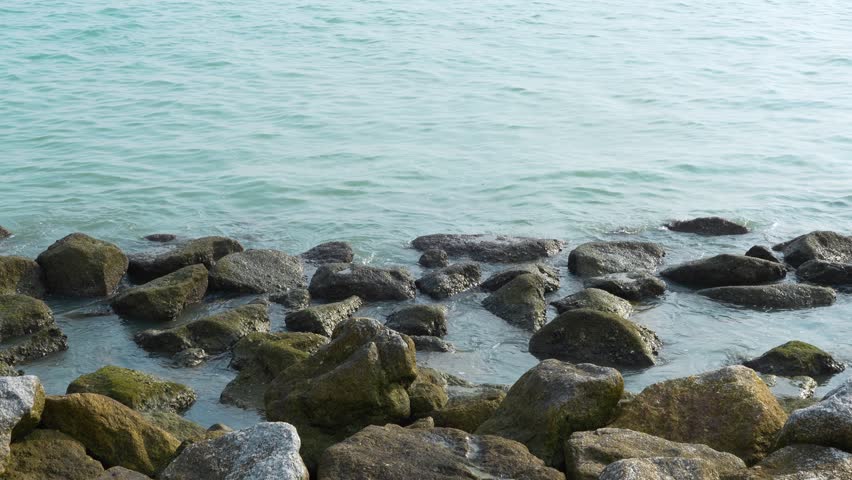 Calm sea waves gently washing over mossy rocks along the coastal shoreline in George Town, Penang, Malaysia.