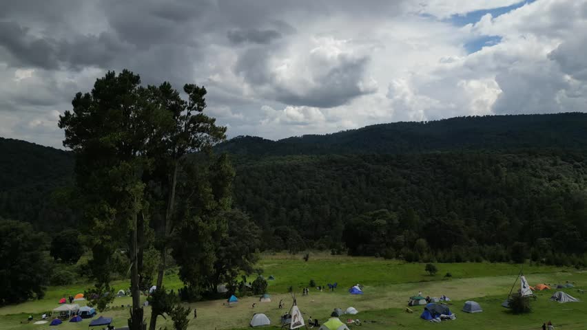 A wide forested landscape under heavy clouds, showing dense green hills before rainfall