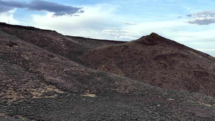 Low altitude drone video reveals dramatic high-desert mountains formed by ancient rhyolite lava flows near Picabo, Idaho. Rugged volcanic terrain in striking evening light. Aerial footage.