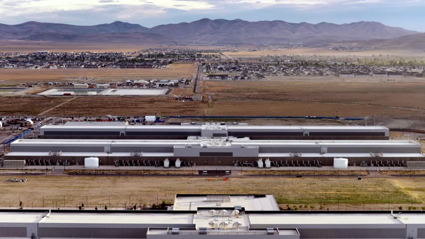Aerial flyover of a Data Center, revealing sprawling facilities, distant Utah town of Eagle Mountain, and dramatic mountain backdrop under soft, natural morning light.