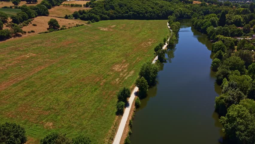 Mayenne River flows beside a riverside towpath, hay meadow and riparian woodland near Change, Mayenne, Pays de la Loire, France, revealing drought-stressed summer grassland across a broad floodplain,