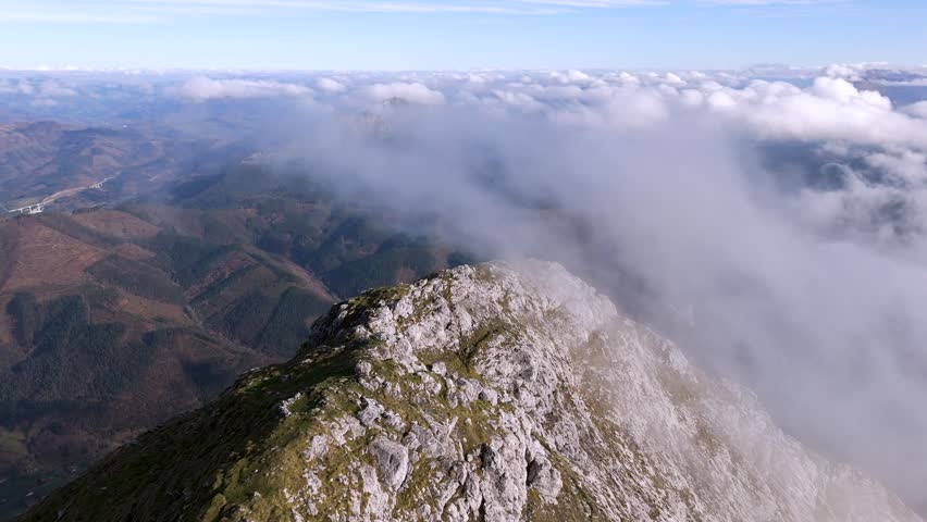 An aerial view of clouds flowing over a rocky mountain ridge in the Basque Country, Spain