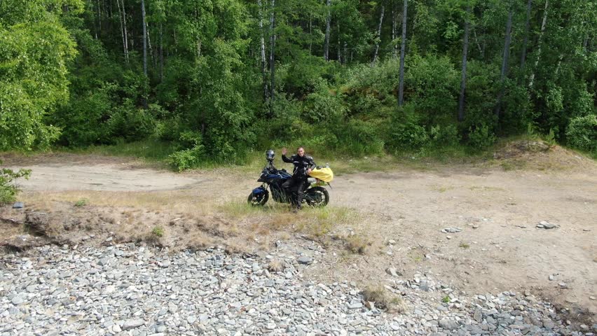 Aerial view of a man on a motorcycle stopping near a rocky shore and green forest, Lake Baikal, Buryatia, Russia.