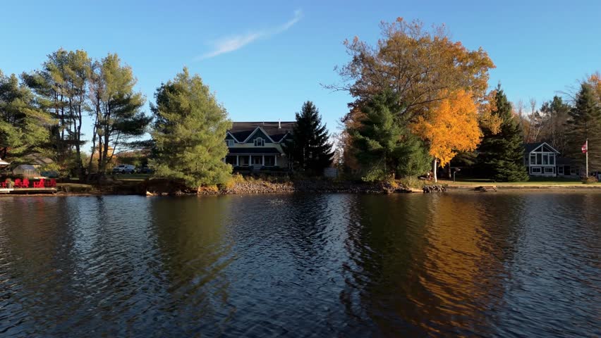 A view of riverside cottages and colorful autumn trees under clear blue sky in Bracebridge, Ontario, Canada
