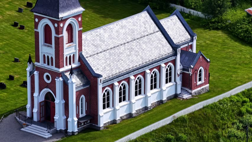 Red brick church with white trim surrounded by grass and cemetery, aerial