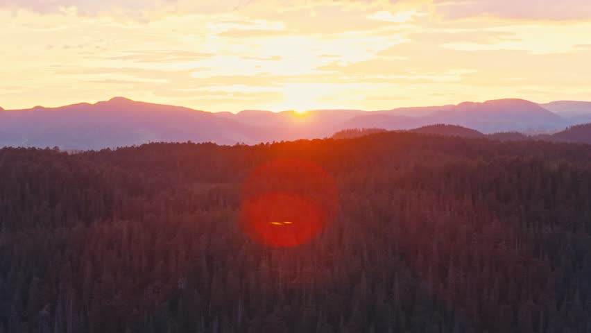 Bright Red Sunlight Illuminates A Mountain Silhouette And Surrounding Forest Landscape. Aerial Shot
