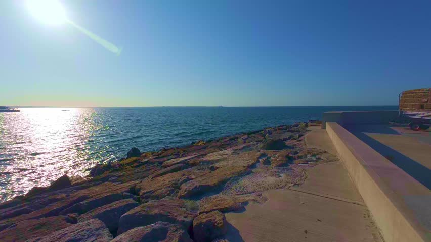 Slow motion sun shining brightly over sea horizon on rocky coast