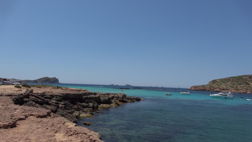 Scenic panoramic landscape showing crystal clear turquoise water of Mediterranean Sea with luxury boats anchored near cliffs during sunny summer day on Balearic island of Ibiza Spain.