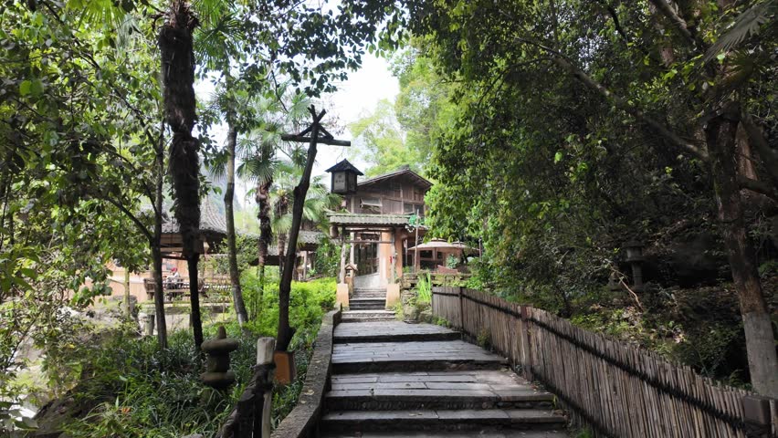 Wangxian Valley, China, 04 April 2026 — Stone stairway path leads through lush spring greenery toward a traditional wooden torii gate and ancient Chinese village buildings.