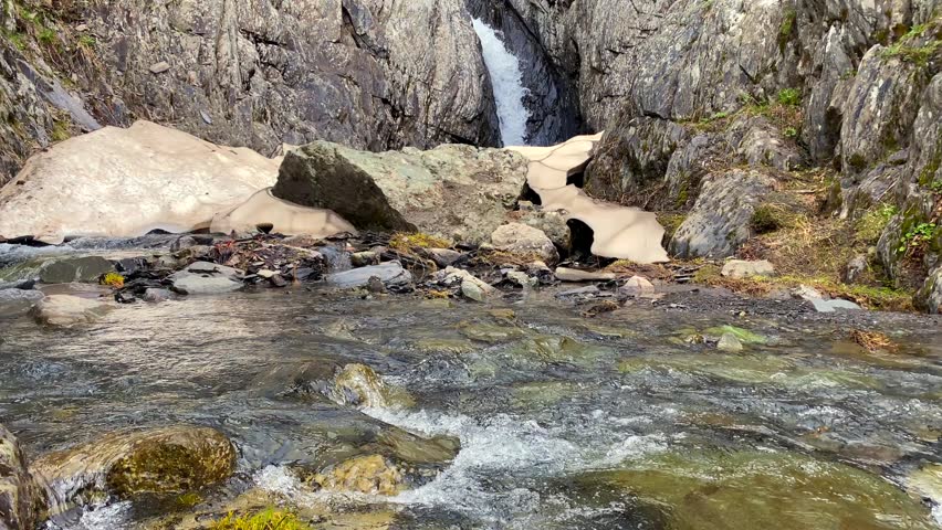Mountain waterfall flows through a narrow rocky gorge near Chaukhi Pass in Georgia, supplying an alpine stream during seasonal snowmelt and supporting wilderness travel and regional ecotourism.