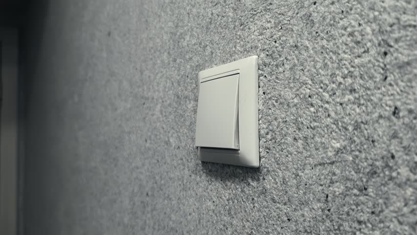 Close up view of contemporary white light switch mounted on rough grey wall surface, displaying moment of illumination activation inside interior space of building hallway.