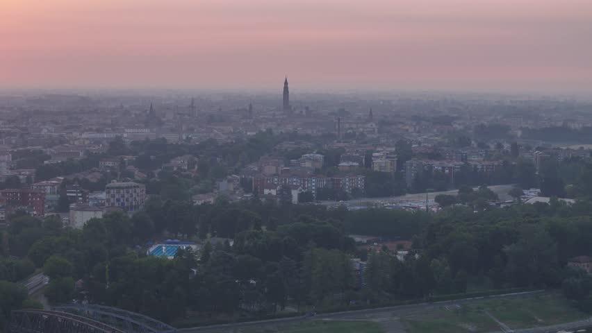 Cremona skyline unfolds around the Torrazzo and Cathedral complex in Cremona, Lombardy, Italy, above the Po Valley under warm evening haze, drone pullback.