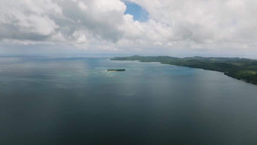 Island coastline with green landscape meeting the calm blue sea under cloudy sky. Siargao, Philippines.