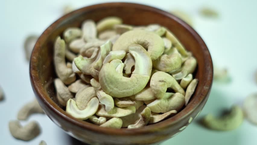 Raw cashew nuts (Anacardium occidentale) piled in a wooden bowl, captured in soft light emphasizing creamy tones, natural curves, and wholesome appeal