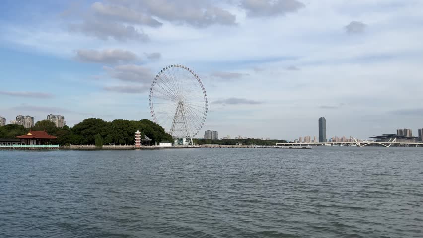 A professional 4K static shot featuring the prominent Ferris wheel at Liyuan Garden in Wuxi, China. The footage captures the intersection of traditional garden architecture and modern urban development across the tranquil waters of Lake Li. With its balanced composition and natural lighting, this clip is highly versatile for travel documentaries, lifestyle content, and geographical projects focusing on East Asian landmarks and Jiangsu province tourism.