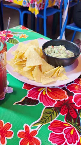 Nachos with guacamole sauce in bowl served in Mexican street restaurant user generated content style vertical video. Tourist or local eating lunch or dinner in authentic place. Foodie or food vlogger