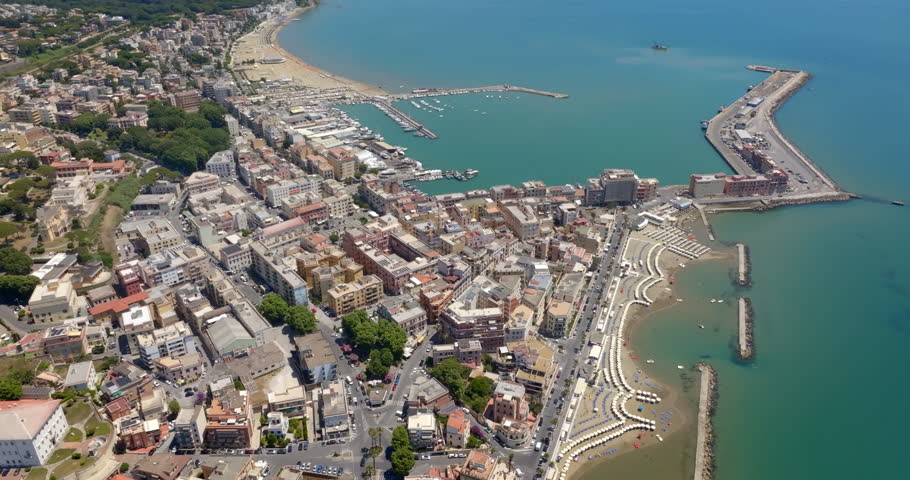 Panorama of Anzio, a city in province of Rome, Lazio, Italy. Aerial view of a sunny coastal town featuring a bustling harbor, long pier, turquoise sea waters, sandy beaches with umbrellas. 
