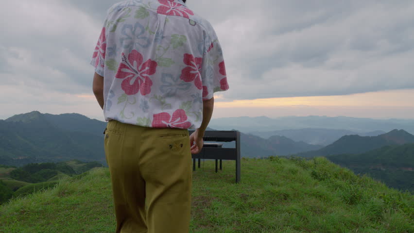 Tracking Shot of Asian Male Musician Starting to Play Piano on Mountain Landscape
