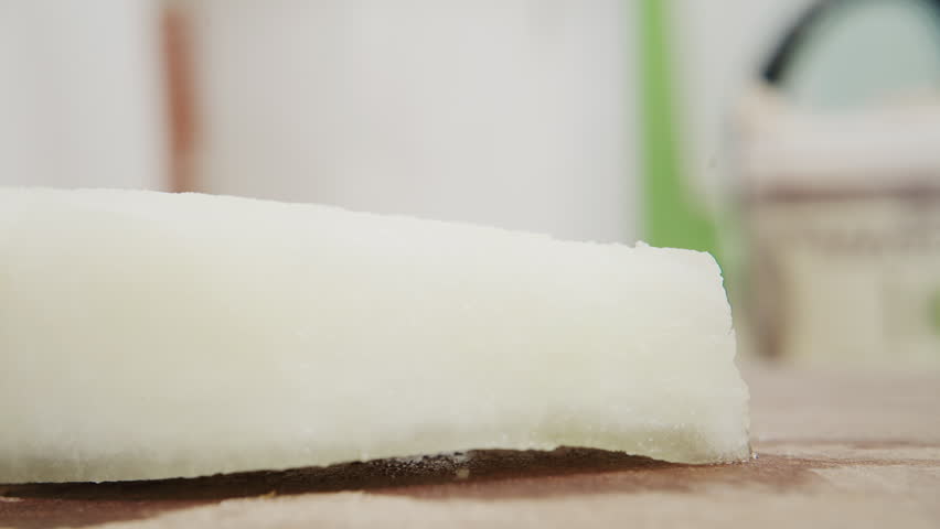 Close up of a knife dicing a white vegetable into cubes on a wooden board in the kitchen