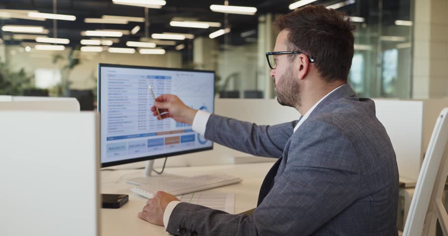 Businessman manager analyst reviewing analytics spreadsheet charts. In office he analyzes data on laptop and screen preparing reports and checking metrics. Core analytics and reporting concept.