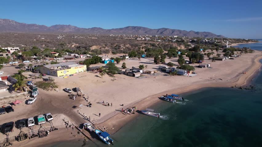 Scenic aerial drone view overlooking a small coastal village beside a calm blue bay in Baja California Sur, Mexico.