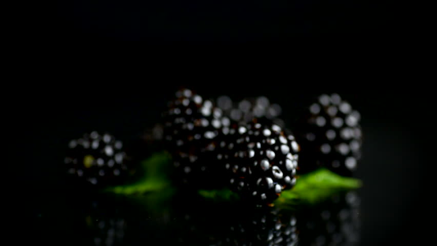 fresh blackberries arranged with green leaves on glossy black surface .