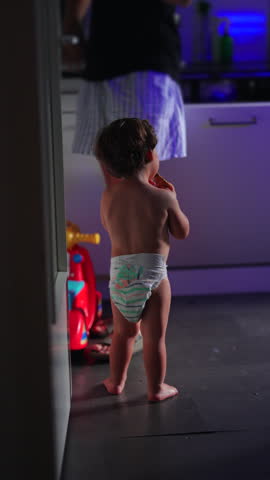Toddler pauses to sit on a ride on toy in the kitchen while carefully eating a snack, capturing independent eating, self directed exploration, childhood curiosity, fine motor development, everyday routine and authentic home moments