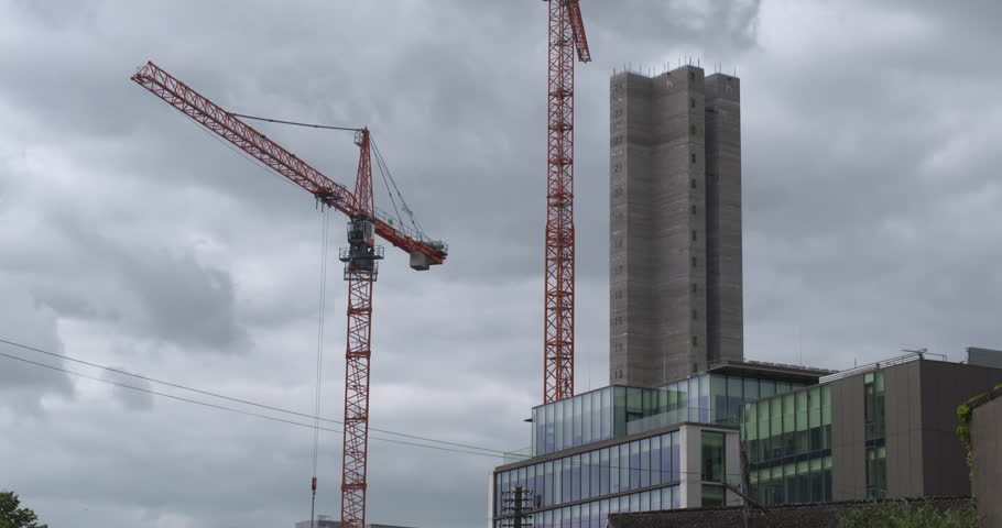 Two large cranes next to tower skyscraper building under construction boom arm rotates