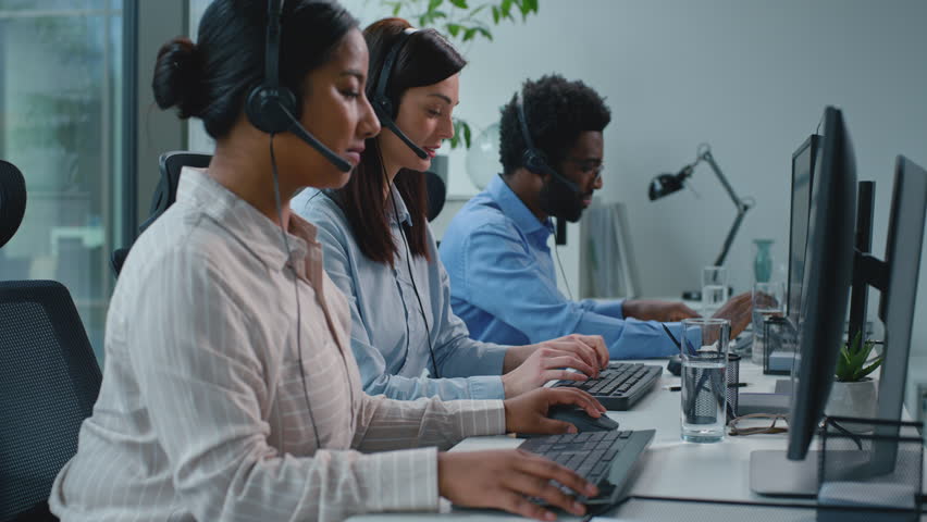 Team of three multiethnic business coworkers working in call center African woman asking help advice talking with Caucasian female writing notes. Two multiracial colleagues teamwork in callcenter