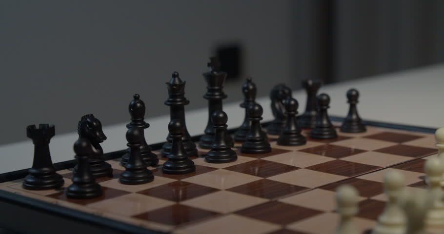 A close up shot of a hand moving a black chess piece on a chessboard, showcasing the intensity of a chess game.