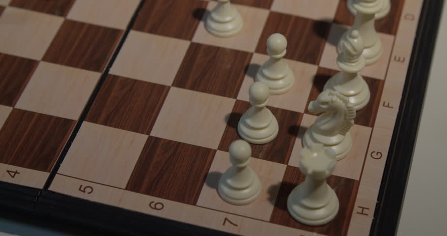A close up shot of a hand moving a chess piece on a wooden chessboard, showcasing the strategic game of chess.