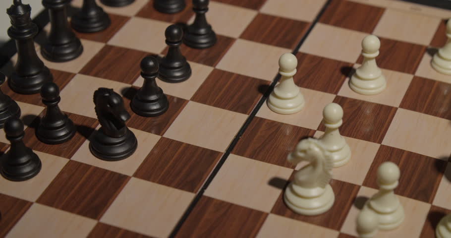 A close up shot of a hand moving a black chess piece on a wooden chessboard, showcasing the intensity of a chess game.