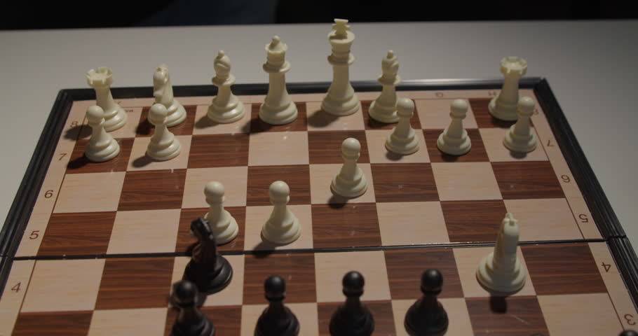 A close up shot of a hand moving a white chess piece on a wooden chessboard during a game. The focus is on the strategic movement of the pieces.