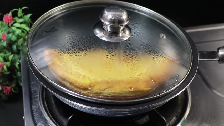 Person removing lid and lifting a fluffy golden omelet from a frying pan