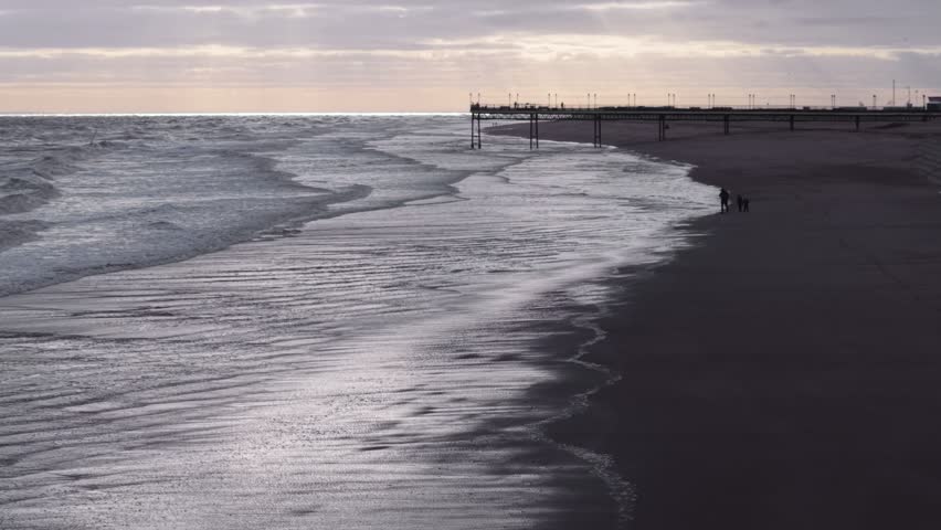 A wide-angle shot of sunrise waves washing over reflective wet sand on Skegness beach, England, under dramatic clouds with cold winter light
