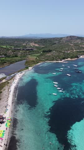 Corsica, France aerial drone view of a curved turquoise bay with pale shoreline and dark underwater reef patterns along the Mediterranean coast.