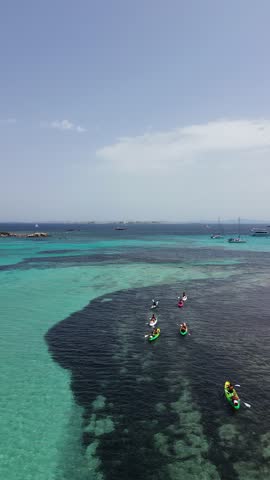 Kayak explore Corsica, France, gliding across transparent turquoise water beside a rugged rocky shoreline.