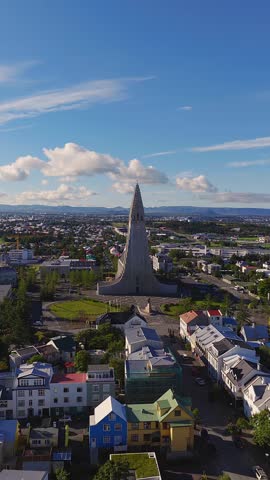 Aerial view of Hallgrimskirkja in Reykjavik, Iceland. The camera glides forward and downward, showing the plaza, houses, tree lined streets, and mountain ridges.