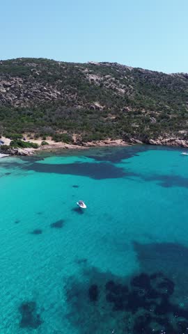 Rotating aerial footage of Corsica, France captures a turquoise coastal bay, rocky shoreline and lush green hills.