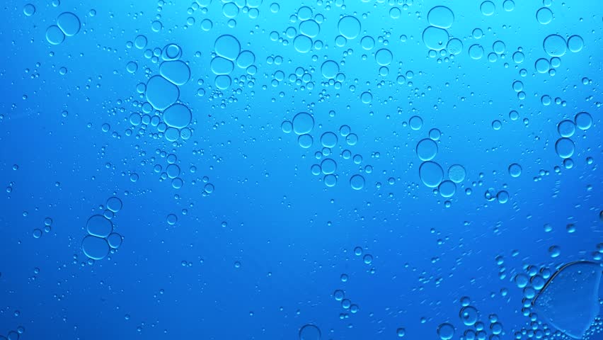 Blue abstract background with oil bubbles floating on water surface in a slow motion macro shot