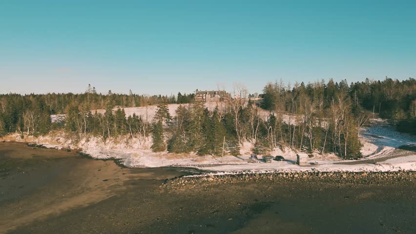 An aerial view of Ministers Island, revealing forested hills, snow-covered terrain, and historic structures in New Brunswick, Canada