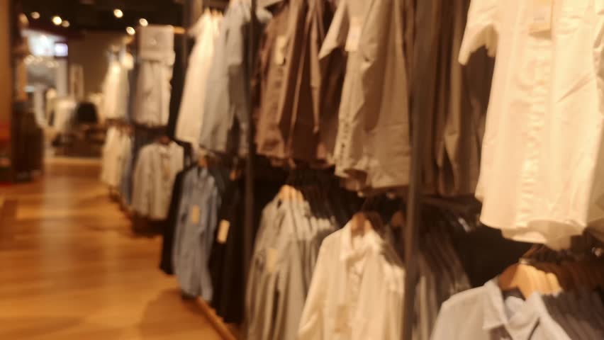 Blurred Defocused Clothing Store Interior with Hanging Shirts and Shoppers Background, Warm Retail Bokeh Backdrop