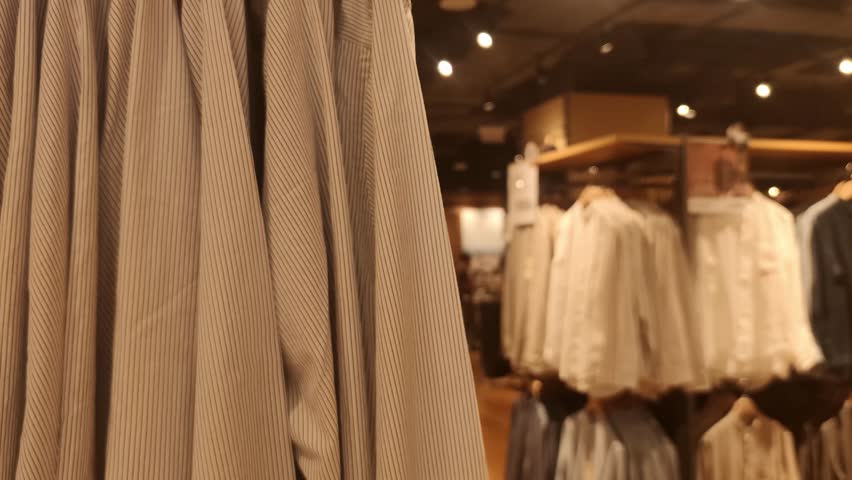 Blurred Defocused Clothing Store Interior with Hanging Shirts and Shoppers Background, Warm Retail Bokeh Backdrop