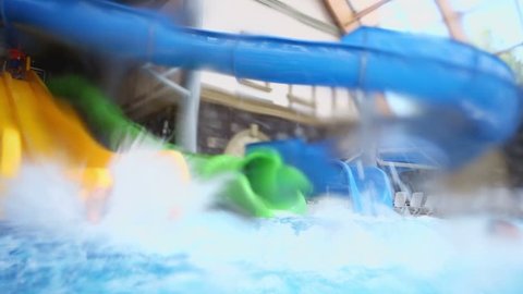 Two kids slid from big colorful water slides in pool at indoor aqua park.