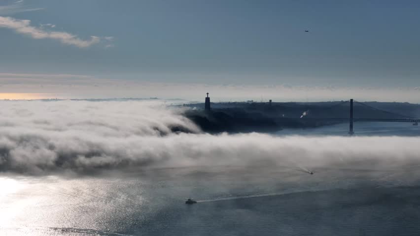 A Drone shot of fog above the River Tejo in Lisbon and Ponte 25 de Abril bridge rises above the mist