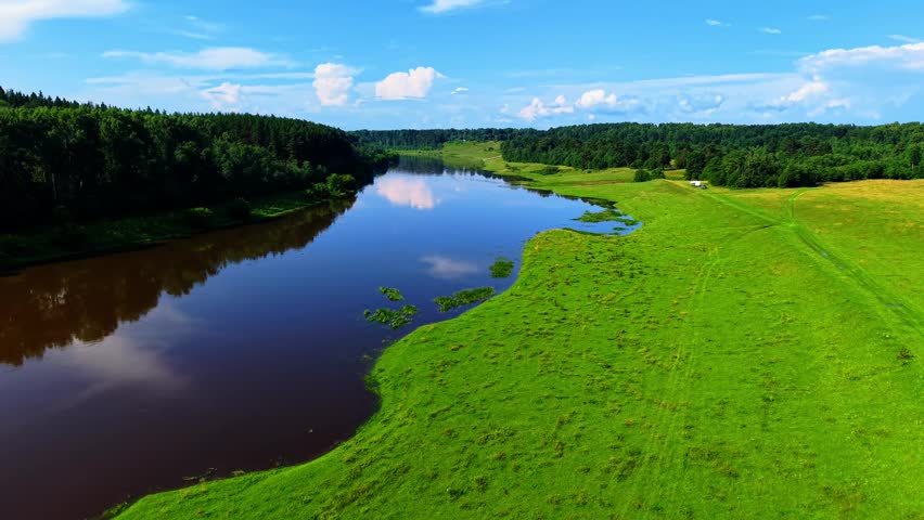 Aerial view of tranquil riverbank under blue skies with lush green surroundings