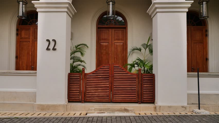 Symmetrical front view of an elegant colonial-style white building entrance with wooden doors, a louvred wooden gate, and house number 22.